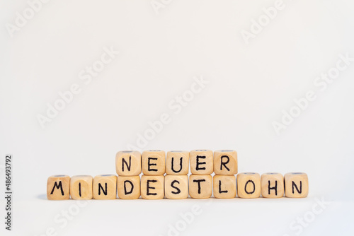 2022 German word for Minimum wage, MINDESTLOHN, spelled with wooden letters wooden cube on a plain white background with banknotes, concept image