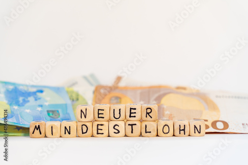 2022 German word for new minimum wage, NEUER MINDESTLOHN, spelled with wooden letters wooden cube on a plain white background with banknotes, concept image