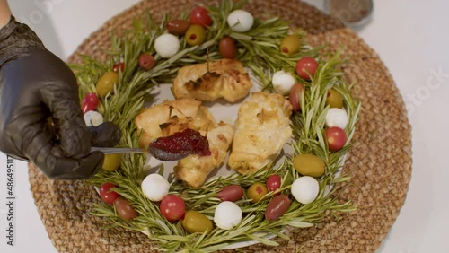 Man’s hands put cranberry sauce on the cooked Chicken Rolls on the Christmas decorated plate