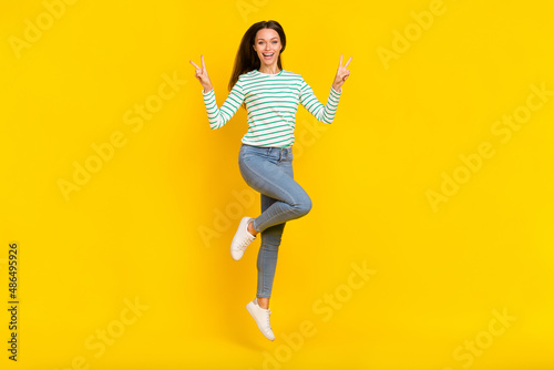 Full length photo of young girl jump up show fingers peace cool v-symbol vacation isolated over yellow color background