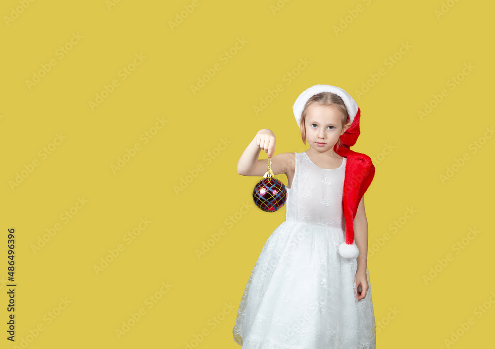 Fototapeta premium Adorable caucasian girl with a Christmas toy in hand looking at the camera.