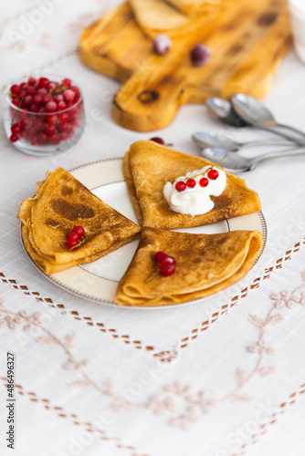 Russian traditional pancakes or blini with sour cream and red currant berries on table laid for Maslenitsa holiday or carnival   