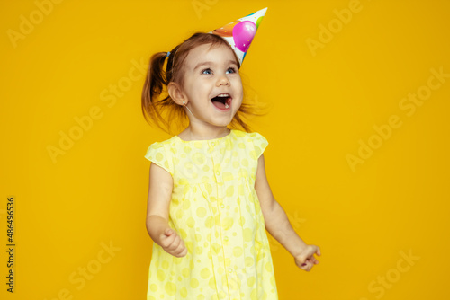 Happy baby girl in princess hat at birthday party spread her arms up screaming isolated on yellow background, baby birthday.