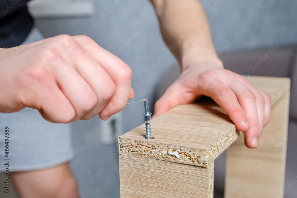 Obraz premium Close-up hands of unrecognizable craftsman using screwdriver and screw for assembling wooden furniture drawer during renovation in home