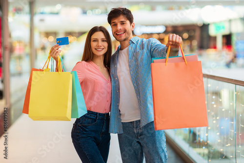 Spouses Showing Credit Card And Shopper Bags Shopping In Mall