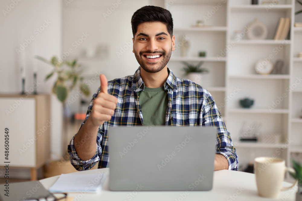 Portrait of smiling Arab man using laptop showing thumbs up Portrait of smiling Arab man using laptop showing thumbs up