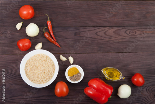Rice, vegetables and spices for cooking jollof rice on brown wooden background. Copy spaes.