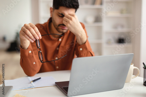 Bored Asian male worker sitting at desk with pc photo