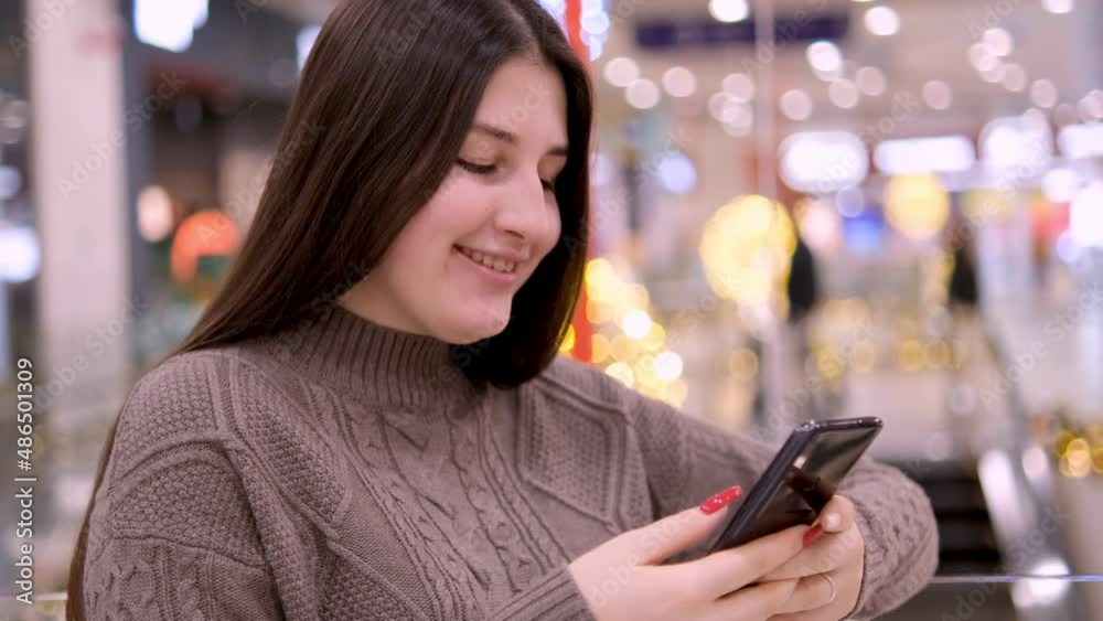 custom made wallpaper toronto digitalThe girl in the shopping center looks into the phone and smiles. Young female hands touch the phone. Woman in a sweater with a smartphone. Clicking, scrolling, watching videos, content, blogs. Modern