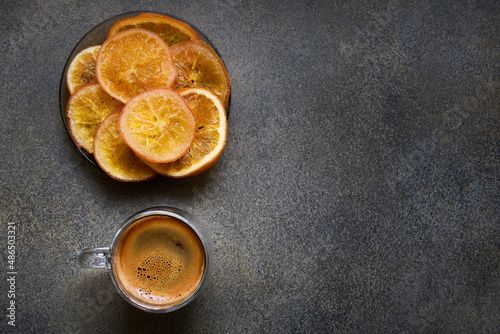Glass double espresso coffee cup and plate with dried orange slices, top view, space for text
