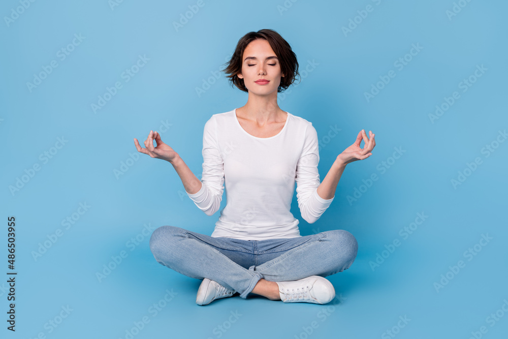 Photo of sweet adorable lady dressed white shirt smiling sitting legs crossed practicing yoga isolated blue color background Photo of sweet adorable lady dressed white shirt smiling sitting legs crossed practicing yoga isolated blue color background