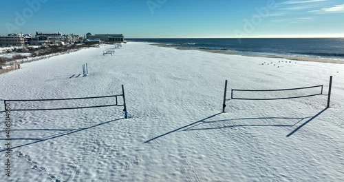 Beach volleyball court nets on sandy beachfront covered in snow. Atlantic Ocean waves on sunny day. photo