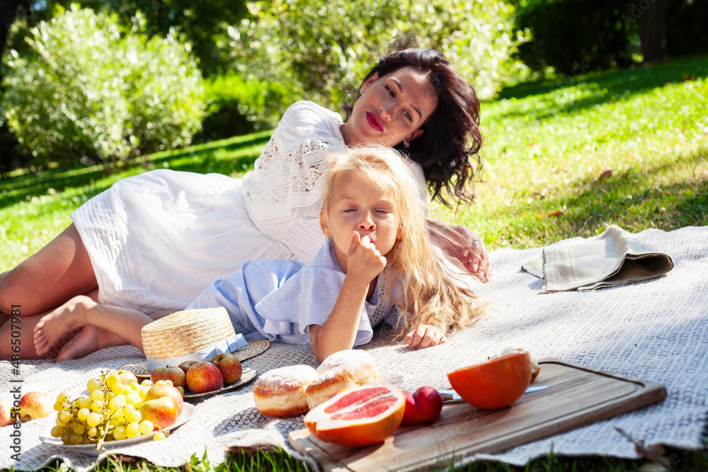 young pretty pregnant brunette woman having fun with her daughter on picnic on green grass in park, lifestyle people concept