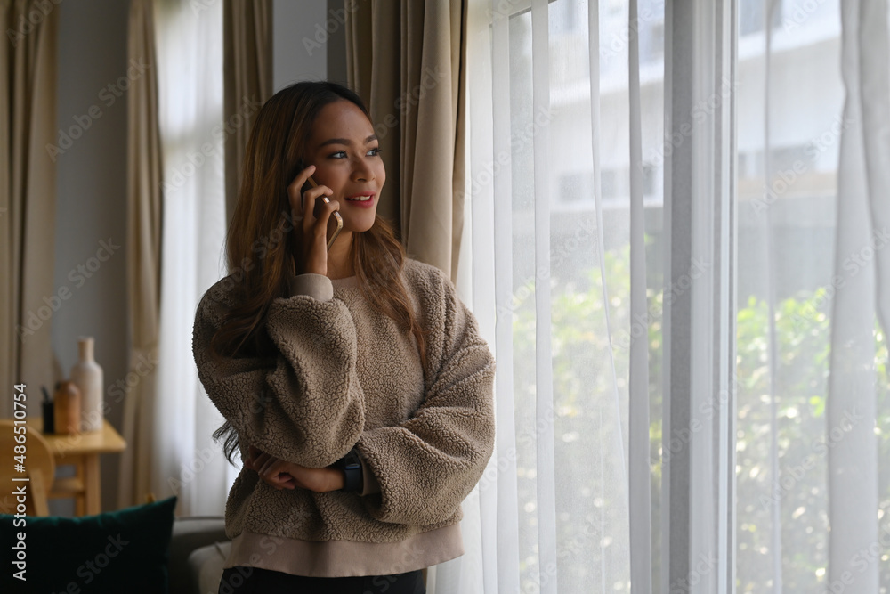 Happy Asian woman staying home wearing a sweat shirt, holding a cup of coffee and talking on a phone. for home and technology concept. Happy Asian woman staying home wearing a sweat shirt, holding a cup of coffee and talking on a phone. for home and technology concept.