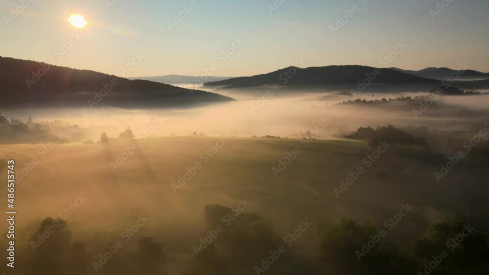 Aerial establishing shot of a beautiful sunrise in a foggy mountain valley flying backward Aerial establishing shot of a beautiful sunrise in a foggy mountain valley flying backward