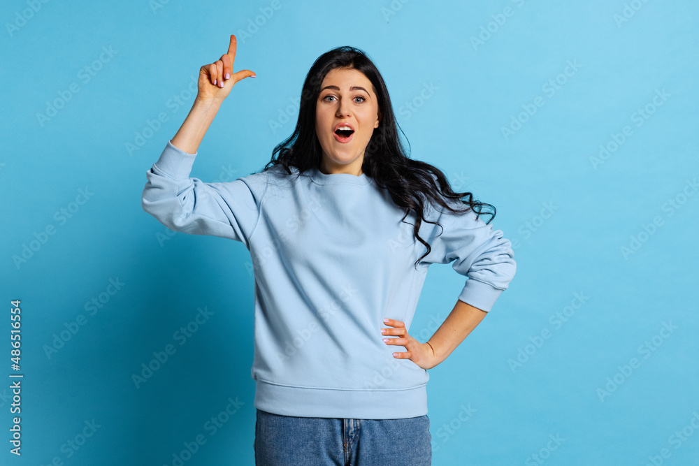 Idea, imagination. Portrait of young beautiful girl with long glossy dark hair posing isolated on blue background. Concept of emotions, facial expression Idea, imagination. Portrait of young beautiful girl with long glossy dark hair posing isolated on blue background. Concept of emotions, facial expression