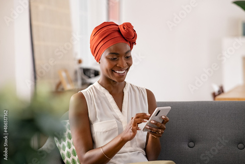 Smiling black woman with african turban using smartphone at home photo