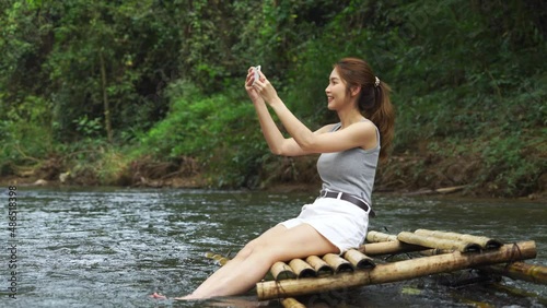 Young asian woman sitting on a bamboo raft taking photos of beautiful view.