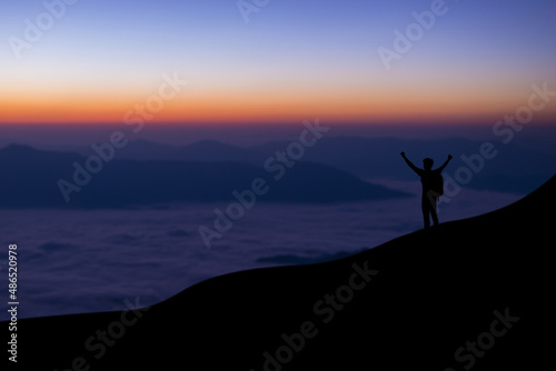 Silhouette of young traveler and backpacker standing and open arm watched foggy landscape and mist alone on top of the mountain. He enjoyed traveling and was successful when he reached the summit.