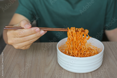 a man in a green t-shirt hold chopsticks with korean style instant noodles. K-pop became a global phenomenon exporting pop culture, entertainment, music, TV dramas and movies. gain immense popularity.