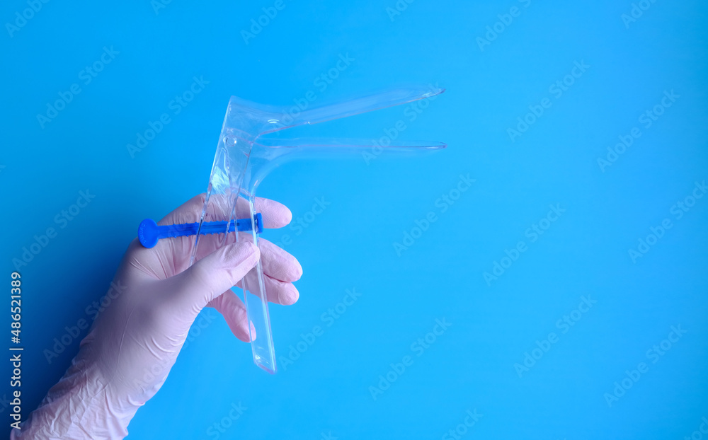 A hand in a pink rubber glove holds a gynecological mirror, a layout with copy space and space for text. A hand in a pink rubber glove holds a gynecological mirror, a layout with copy space and space for text.