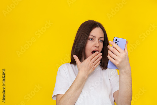 Portrait of a smiling european brunette woman wearing white T-shirt on yellow background talking on mobile phone.