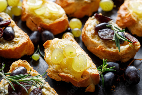 Canapes  from sliced baguette with cheese and grapes, flavored with herbs on a dark background, close-up view.