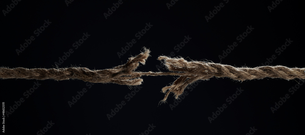 A stretched rope breaks on a black background. The concept of