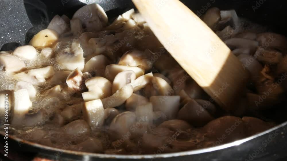 Fried mushrooms in a pan. Wooden kitchen spatula turns over pieces of champignon mushrooms Fried mushrooms in a pan. Wooden kitchen spatula turns over pieces of champignon mushrooms