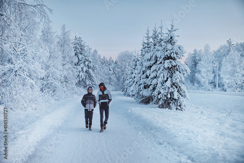 Two boys walking along a snow covered road in winter, Rovaniemi, Lapland, Finland photo