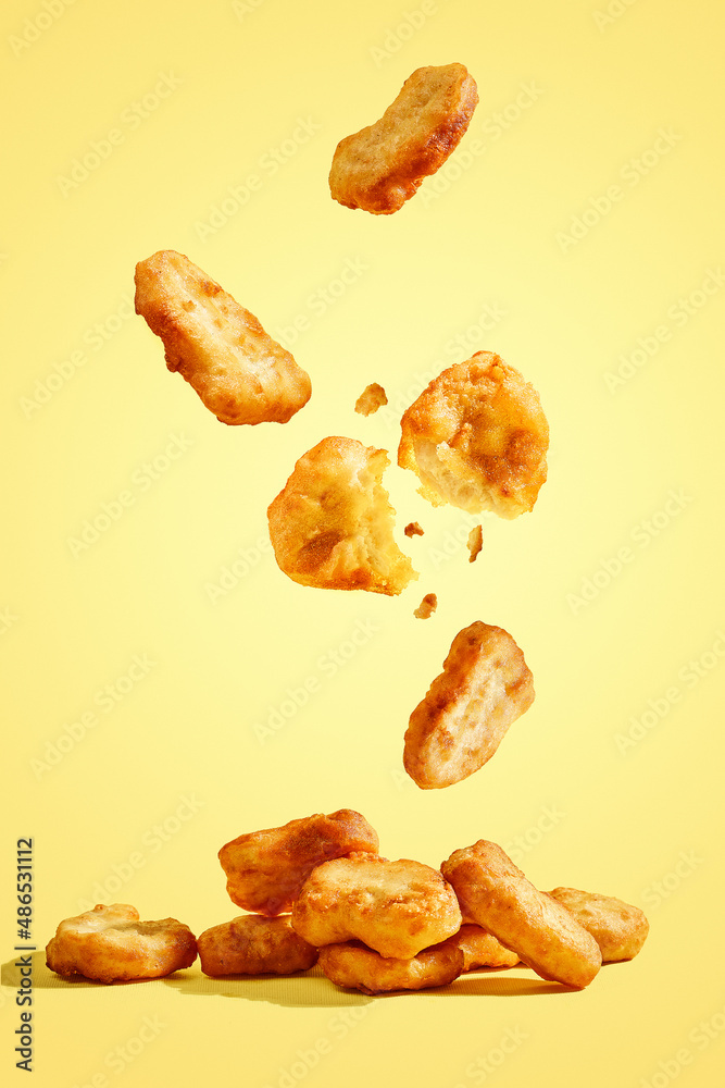 Flying chicken nuggets, one broken in half on yellow background Stock