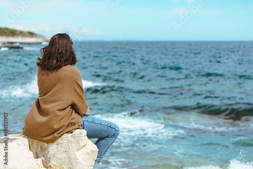 woman sitting on cliff enjoying view of the sea. windy weather. sunny day