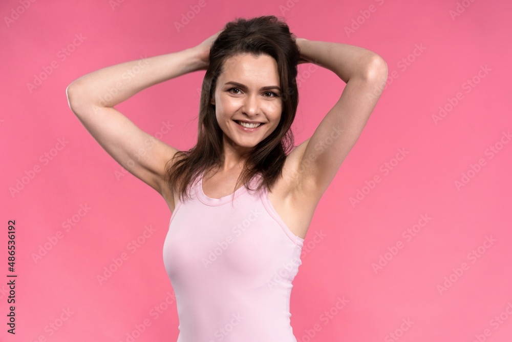 Young brunette woman in sleeveless t-shirt tighten hair back head with hands up isolated on pink background Young brunette woman in sleeveless t-shirt tighten hair back head with hands up isolated on pink background