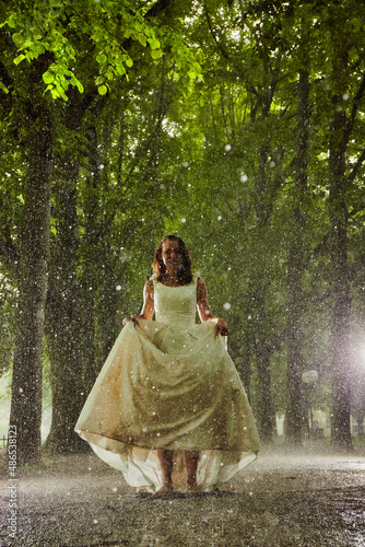 happy bride in a white wedding dress in the rain on an alley under big green trees walking peaying sitting and laughing photo