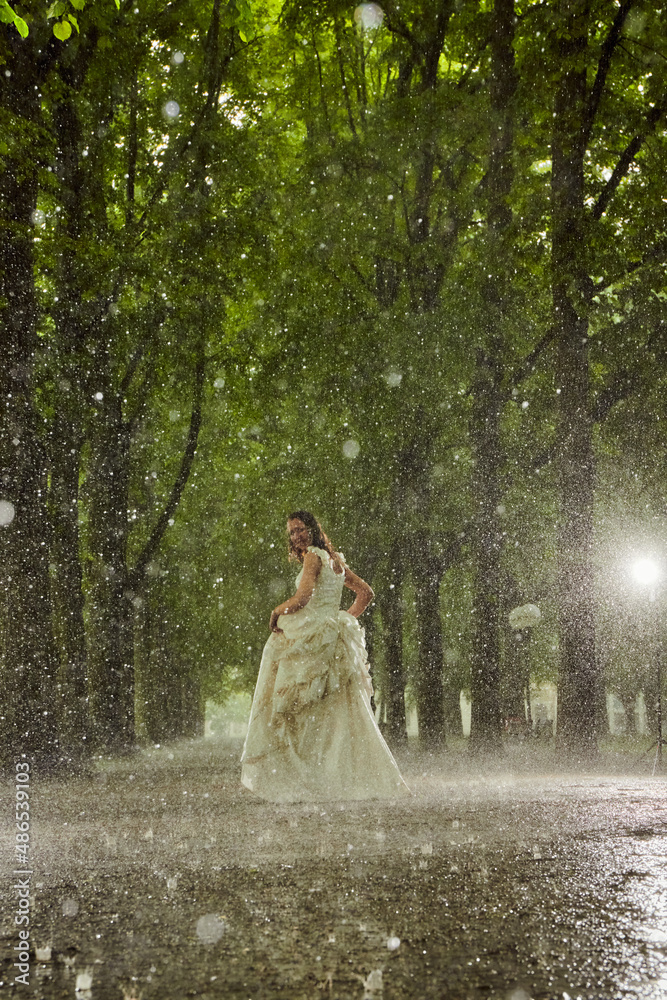 happy bride in a white wedding dress in the rain on an alley under big green trees walking peaying sitting and laughing happy bride in a white wedding dress in the rain on an alley under big green trees walking peaying sitting and laughing