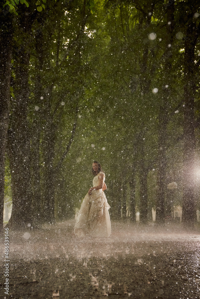 happy bride in a white wedding dress in the rain on an alley under big ...
