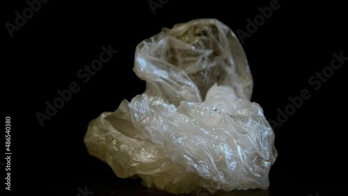 Crumpled empty plastic bag with dirt and drops of condensate. Polyethelene package rotates on stand. Black background at bright illumination macro photo
