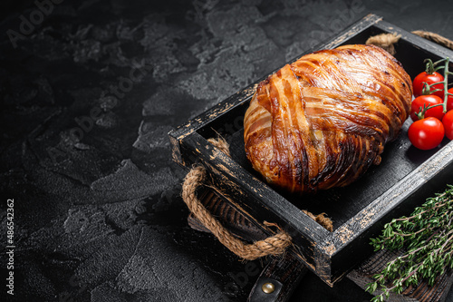 Roast bacon wrapped meatloaf, meat loaf in a tray with herbs. Black background. Top view. Copy space