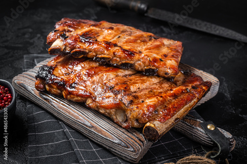 Stack of grilled pork ribs in BBQ sauce on a chopping board. Black background. Top view