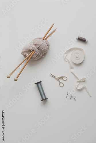 Top view of scissors, threads, knitting needles and sewing supplies on a white background. Concept of craft hobby, knitting and sewing.