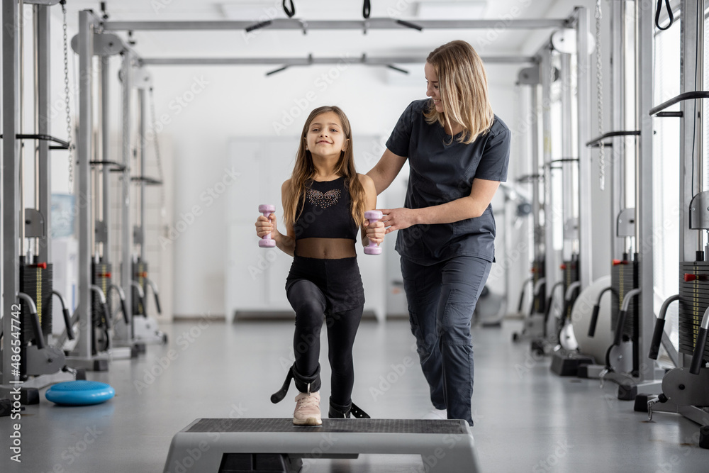 Rehabilitation specialist helping little girl to do exercises at gym