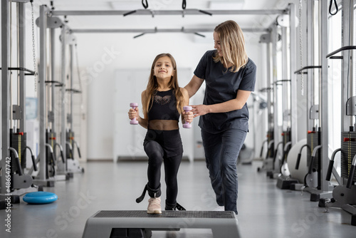 Rehabilitation specialist helping little girl to do exercises at gym. Concept of physical therapy for back health and correct posture for kids © rh2010