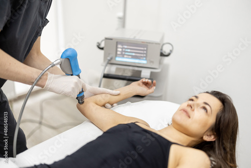 Canvas Print Doctor applies shock wave therapy with special medical equipment on women's elbow joint at medical office