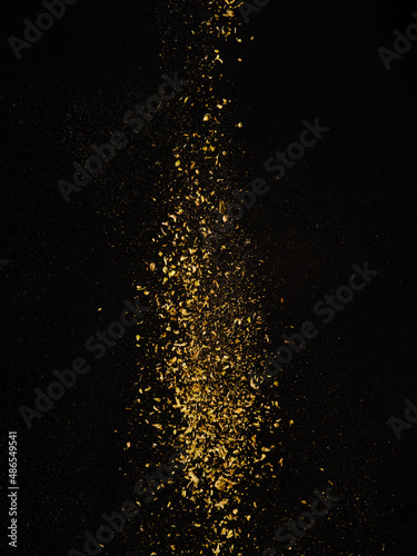 Golden flow of spices and seasonings in frozen flight on a black background. Beautiful composition. Minimalism. There are no people in the photo. Advertising, banner.