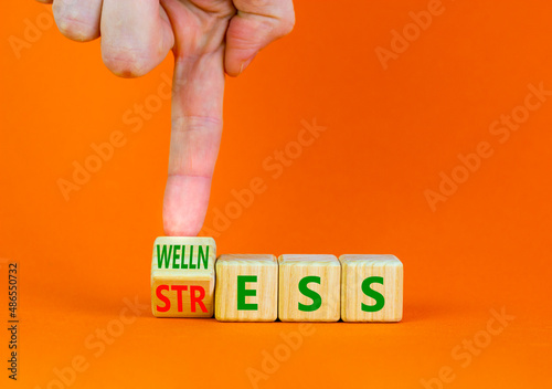 Wellness or stress symbol. Doctor turns the wooden cube and changes the word Stress to Wellness. Beautiful orange table orange background. Medical psychological wellness or stress concept. Copy space.