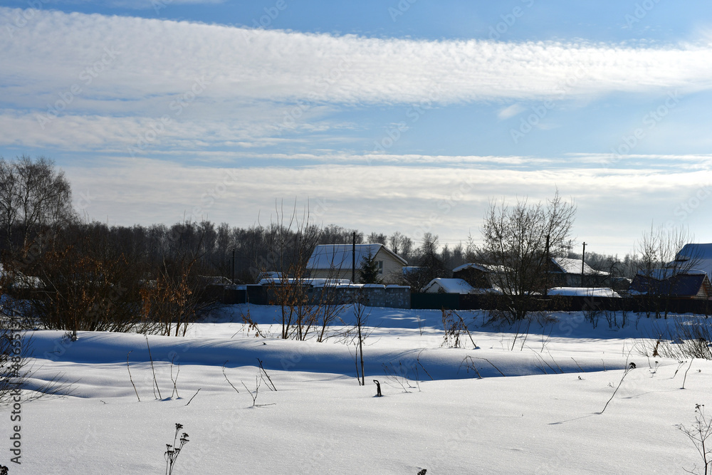 A frosty clear winter day. View of a snow-covered field and a village or cottages in the distance