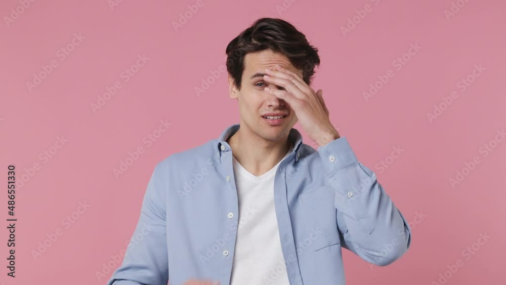 Sad upset worried disturb displeased young brunet man 20s wears blue shirt sigh suspire sithe put hands on face isolated on plain pink background studio portrait. People emotions lifestyle concept Sad upset worried disturb displeased young brunet man 20s wears blue shirt sigh suspire sithe put hands on face isolated on plain pink background studio portrait. People emotions lifestyle concept