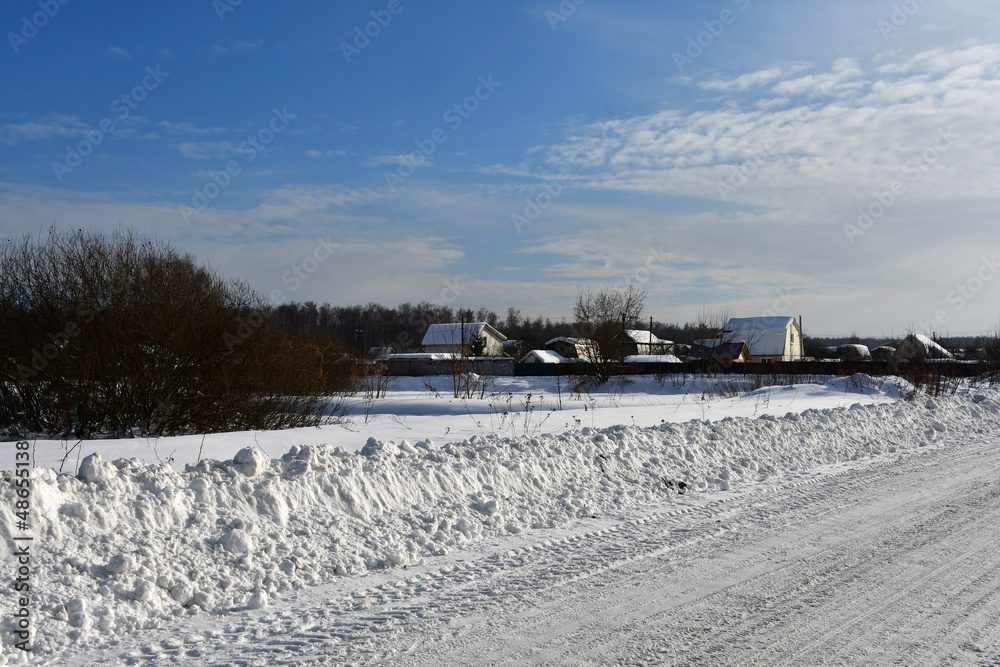 A frosty clear winter day. View of the snowy road leading to the village or country village, rural houses in the distance