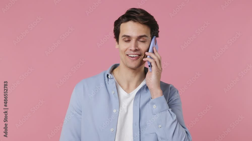 Happy calm smiling cheerful fancy young brunet man 20s years old wears blue shirt hold use talk on mobile cell phone conducting pleasant conversation isolated on plain pink background studio portrait Happy calm smiling cheerful fancy young brunet man 20s years old wears blue shirt hold use talk on mobile cell phone conducting pleasant conversation isolated on plain pink background studio portrait