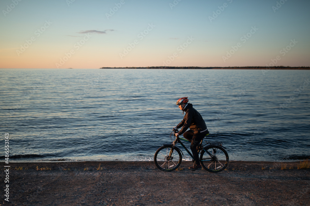 Man riding bicycle along sea at sunset